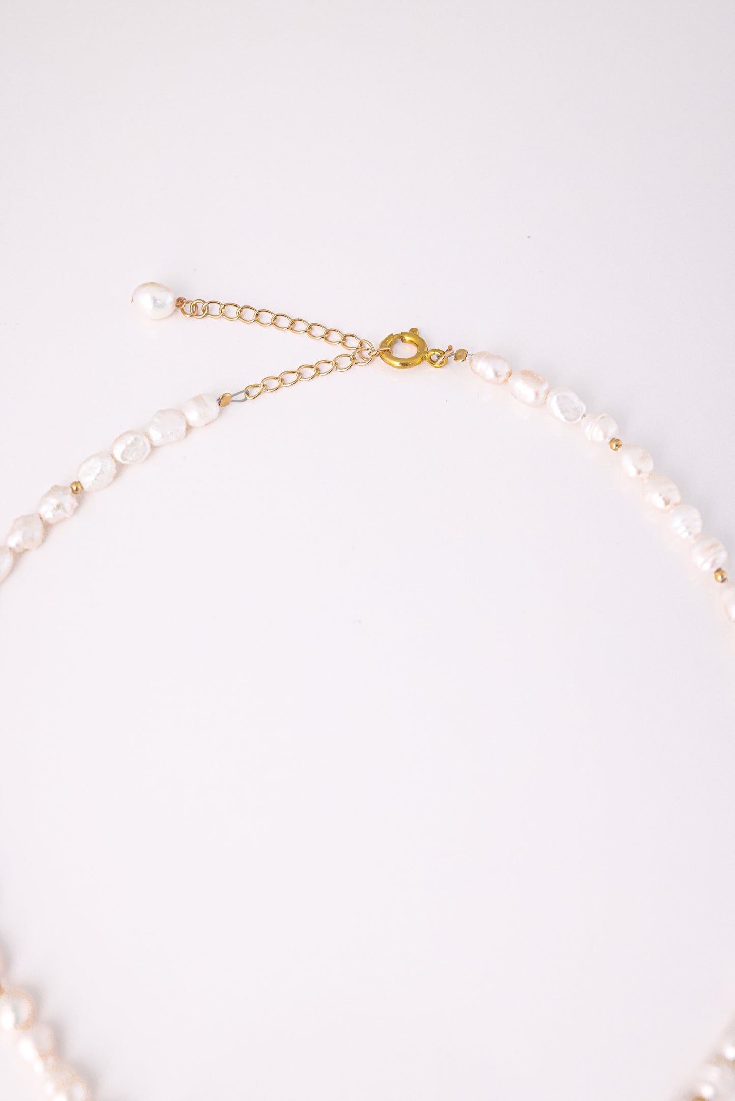 שרשרת BELA NECKLACE GOLD, תקריב על סוגר ושרשרת הארכה מזהב עם פנינה. פנינים לא סדירות משולבות בחרוזי זהב.