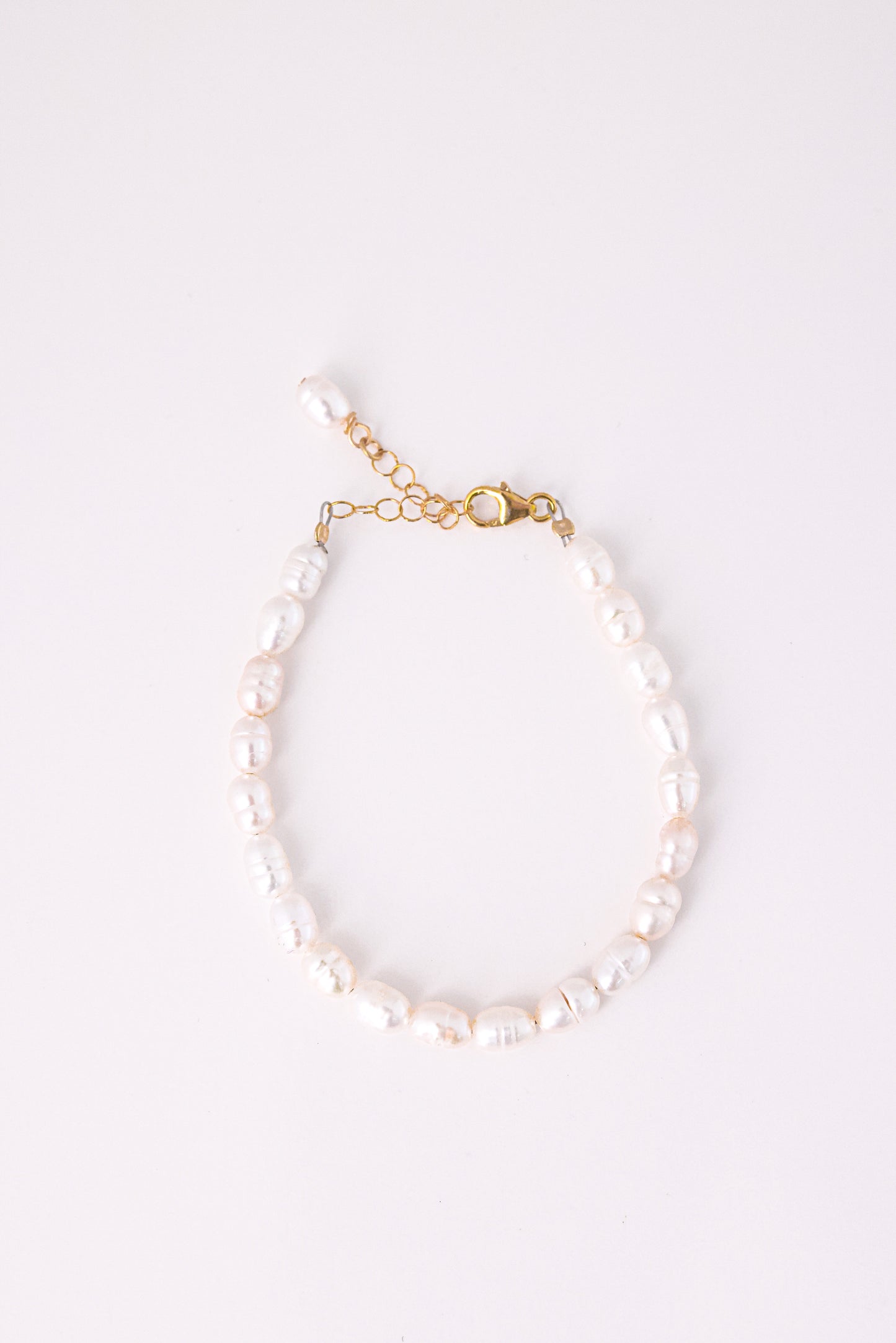 צמיד ANNA BRACELET GOLD, פנינים לבנות לא סדורות, סוגר ושרשרת הארכה מזהב, מצולם מלמעלה על רקע לבן.