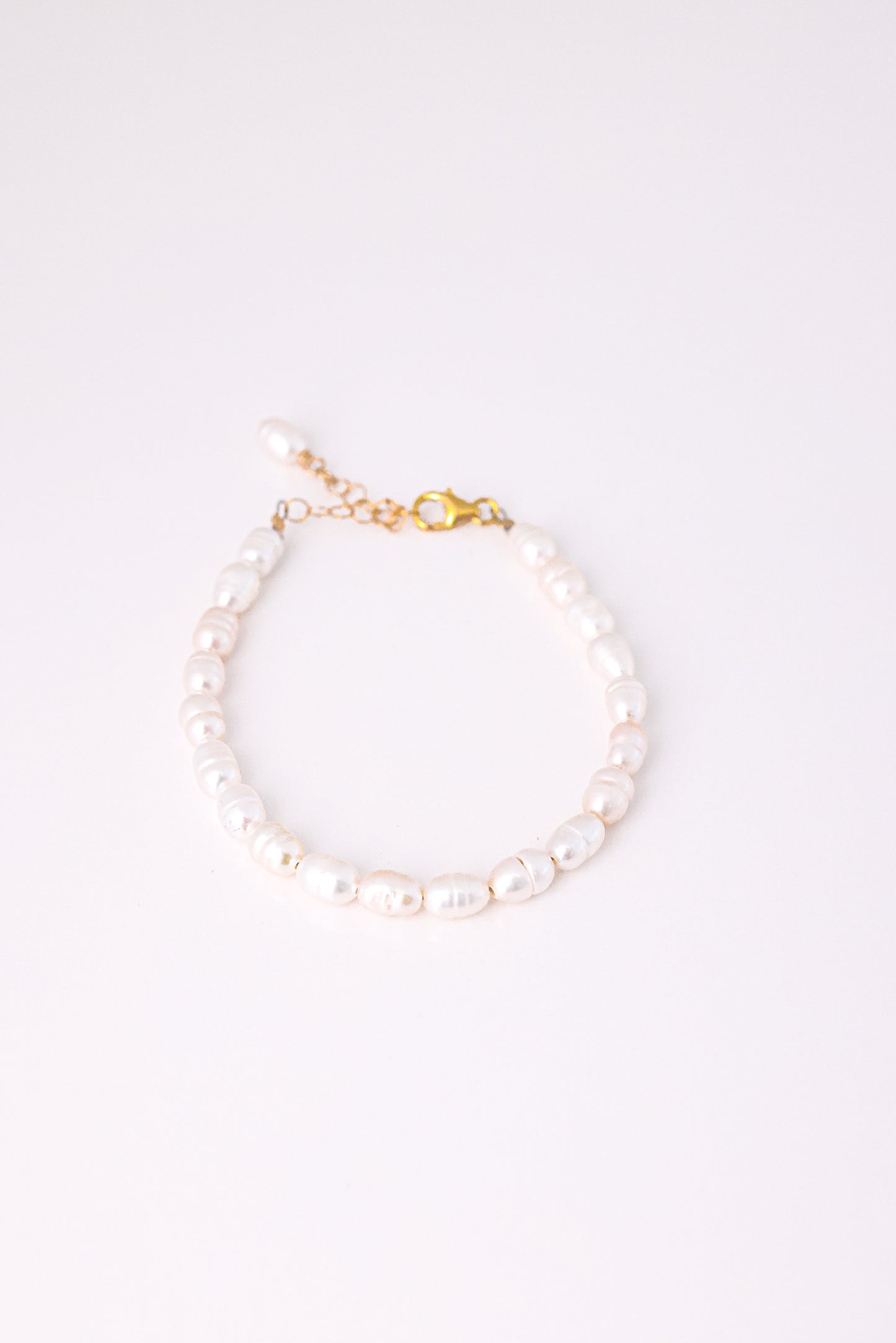 צמיד ANNA BRACELET GOLD פנינים לבנות אובליות, מונח במעגל על רקע לבן, סוגר ושרשרת הארכה מזהב.