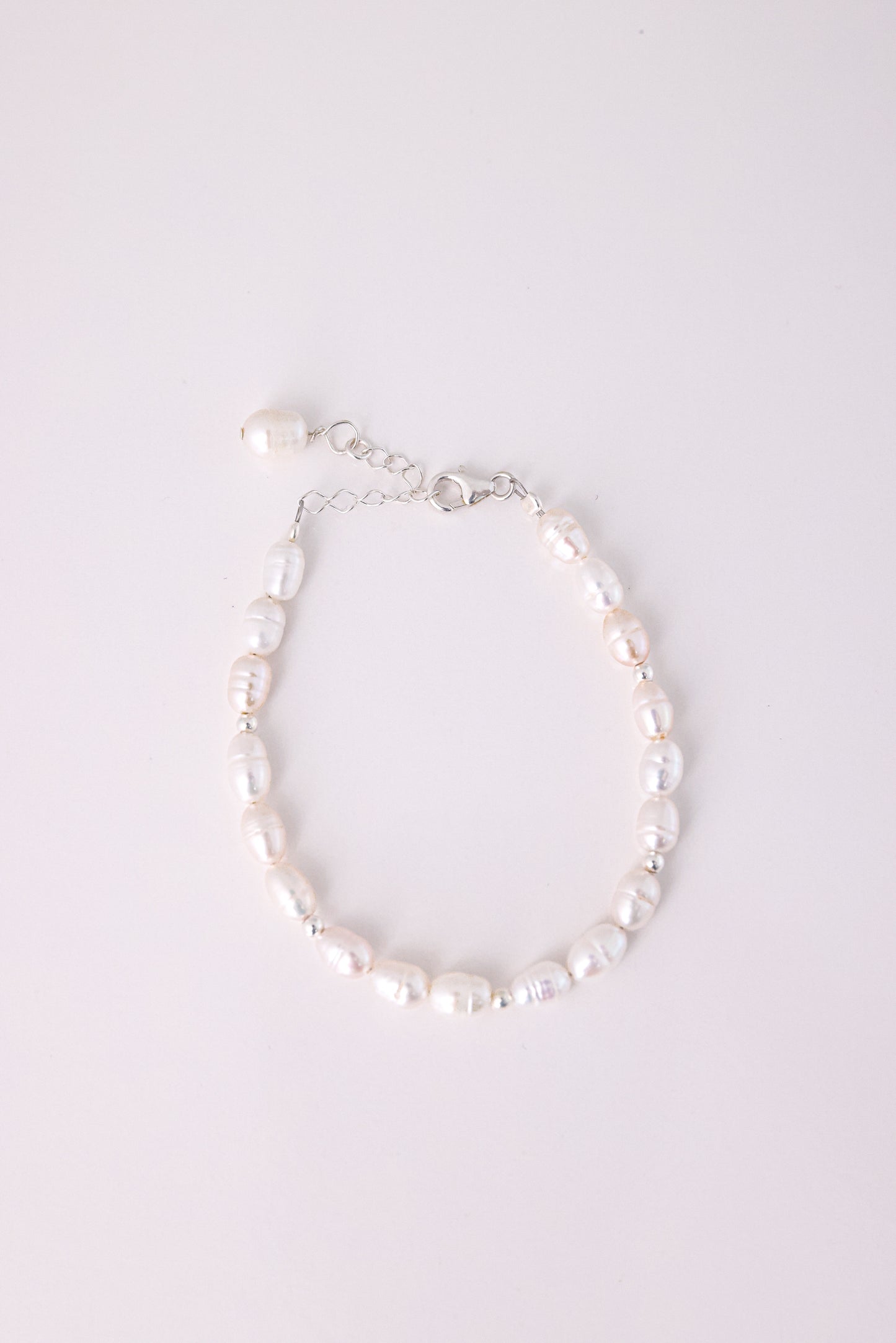 צמיד BELA BRACELET SILVER כסף, מונח שטוח על רקע לבן. תקריב על פנינים לא סדירות, חרוזים קטנים וסוגר עם שרשרת הארכה.