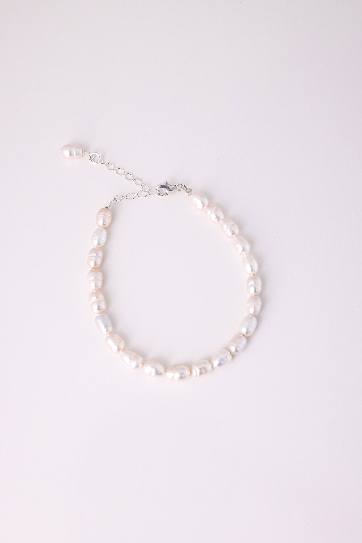 צמיד ANNA BRACELET SILVER פנינים מתורבתות לא סדירות בגוון ורדרד, מצולם מלמעלה עם סוגר ושרשרת הארכה כסופים על רקע לבן.