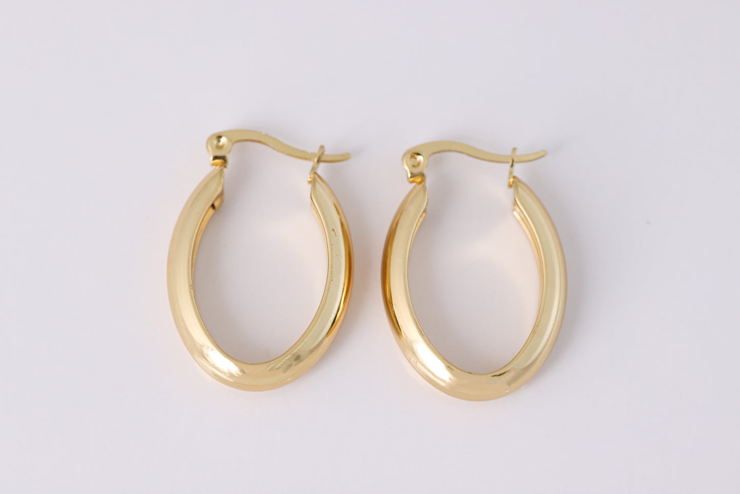 זוג עגילי חישוק EDEN EARRINGS זהב אובליים ועבים, מונחים על רקע בהיר, צילום תקריב.