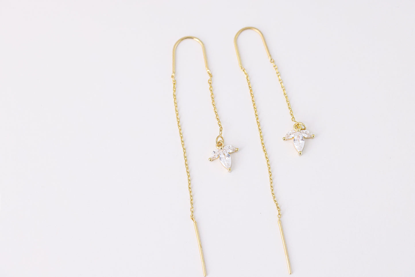 עגילי SARAI מזהב, עיצוב נשפך עם תליון פרח משלוש אבני זירקוניה שקופות. צילום מלמעלה על רקע לבן, מבט מלא.