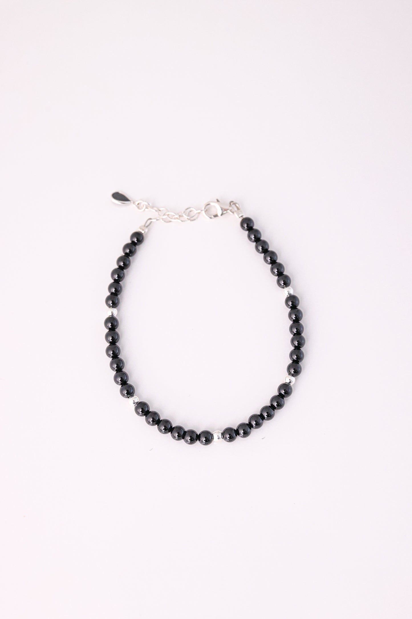 צמיד RONA מעוצב מחרוזים שחורים מבריקים עם חרוז כסף בודד, סוגר ושרשרת הארכה כסופים, מצולם מלמעלה על רקע לבן.