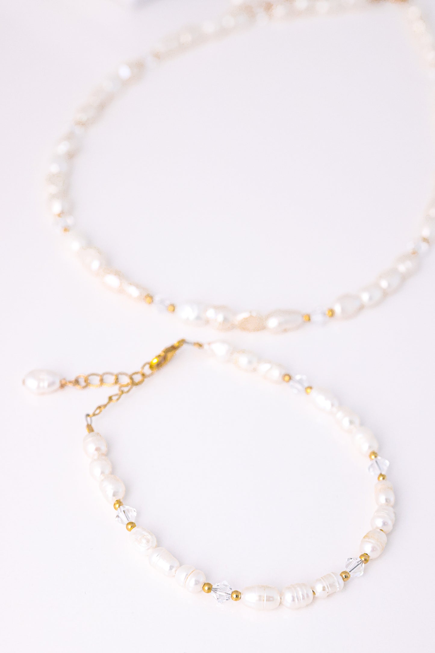 סט תכשיטי ALAMOR QUARTZ GOLD. צמיד פנינים וחרוזי קוורץ שקופים בתקריב עם סוגר זהב, שרשרת תואמת ברקע.