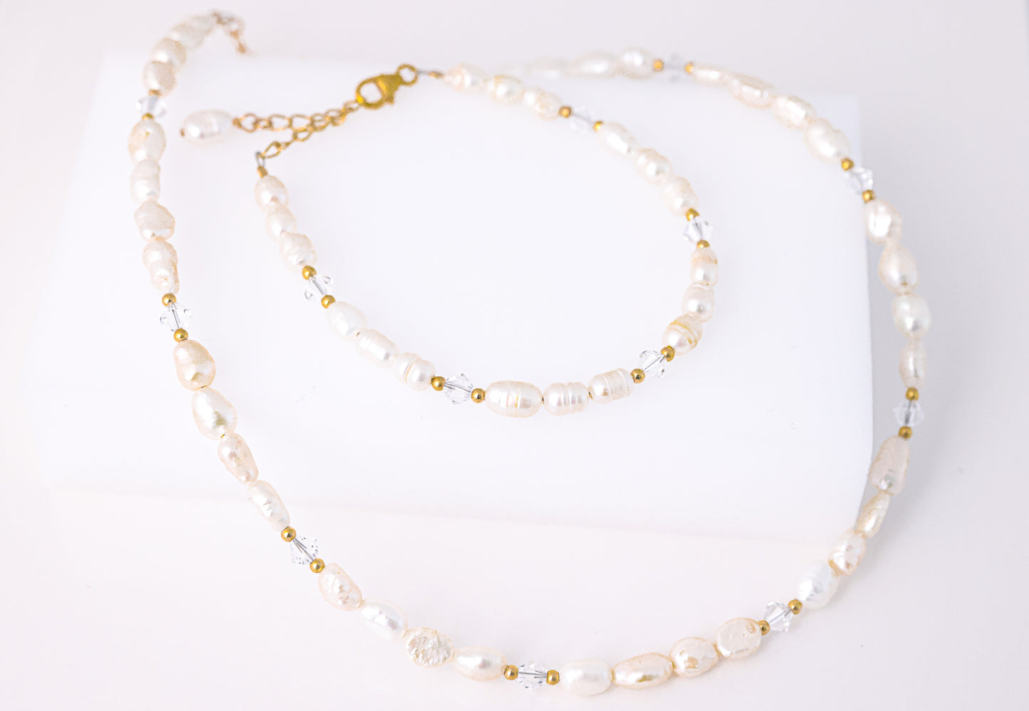 שרשרת ALAMOR QUARTZ GOLD: פניני בארוק, חרוזי קוורץ שקופים וזהב, מונחת בצורת S. מבט עליון על רקע לבן.