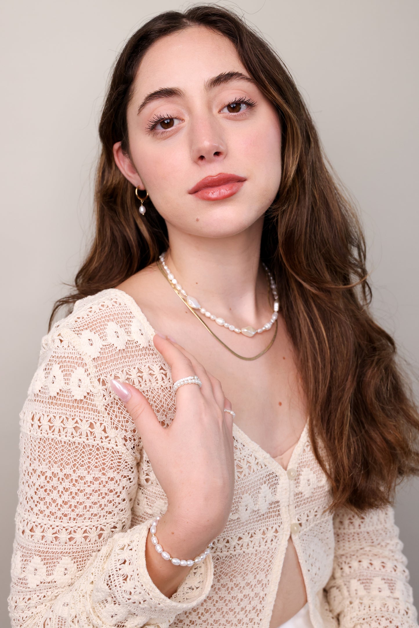 דוגמנית עונדת שרשרת SHAI NECKLACE פנינים טבעיות ושרשרת זהב שטוחה, יד על הכתף.