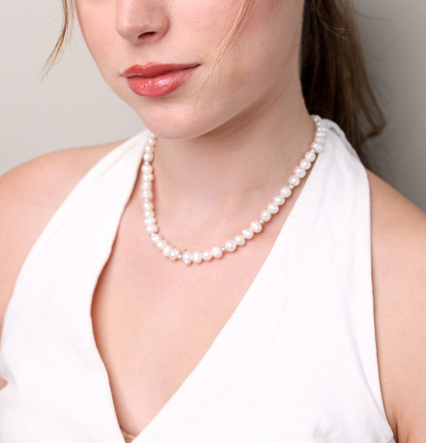 תקריב של שרשרת GEFEN של Lidi, פנינים לבנות וחרוזי כסף על צוואר דוגמנית בחולצת צווארון הלטר לבנה.