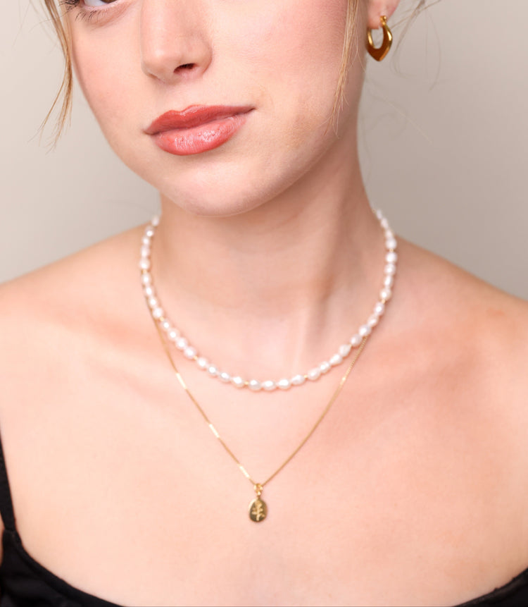 שרשרת BELA NECKLACE GOLD זהב עם תליון עץ על צוואר דוגמנית, בשילוב שרשרת פנינים, תקריב על הדקולטה.