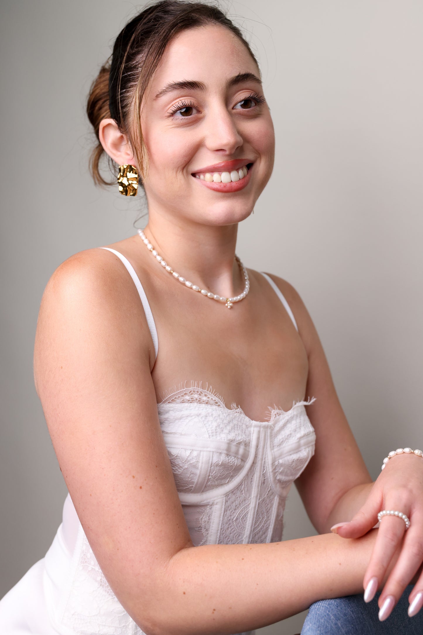 דוגמנית מחייכת במבט צדדי, עונדת שרשרת "NOA NECKLACE GOLD" מפנינים לא סימטריות וחרוזי זהב קטנים.