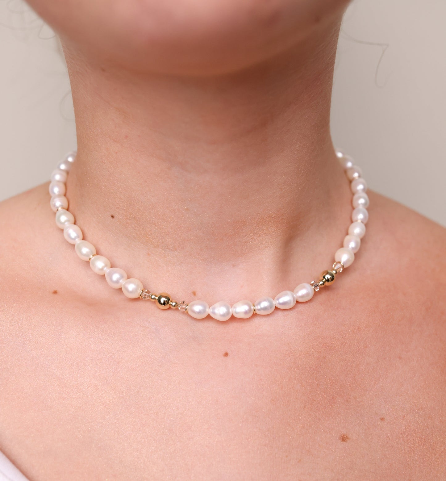 שרשרת קולר ADIA על צוואר דוגמנית, תקריב פניני מים מתוקים לבנות, חרוזי זהב וקריסטל זוהרים.