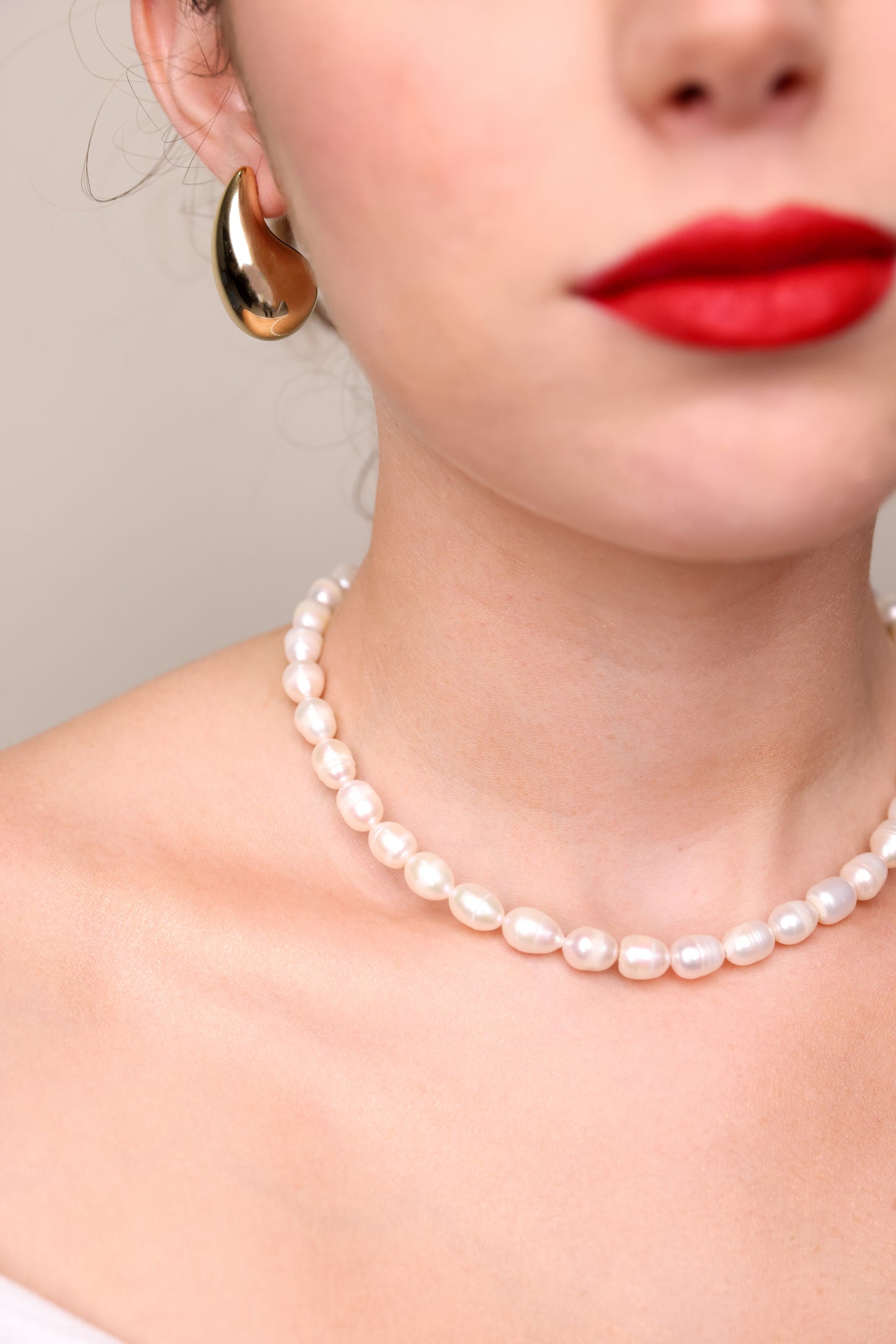 שרשרת AMELIA פנינים טבעיות על צוואר דוגמנית, תקריב אופנתי עם שפתיים אדומות ועגיל זהב.