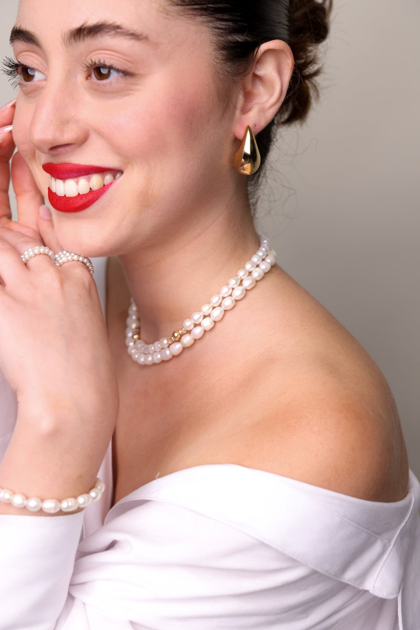 עגילי LOLA L EARRINGS זהב בצורת כיפה מבריקה על אוזן דוגמנית מחייכת, מבט צד תקריב.