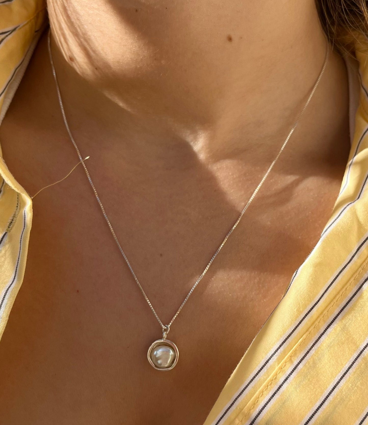 שרשרת LUNA כסף עם פנינה בארוק בחישוק כסף מעוצב, על צוואר דוגמנית וחולצה צהובה מפוספסת.