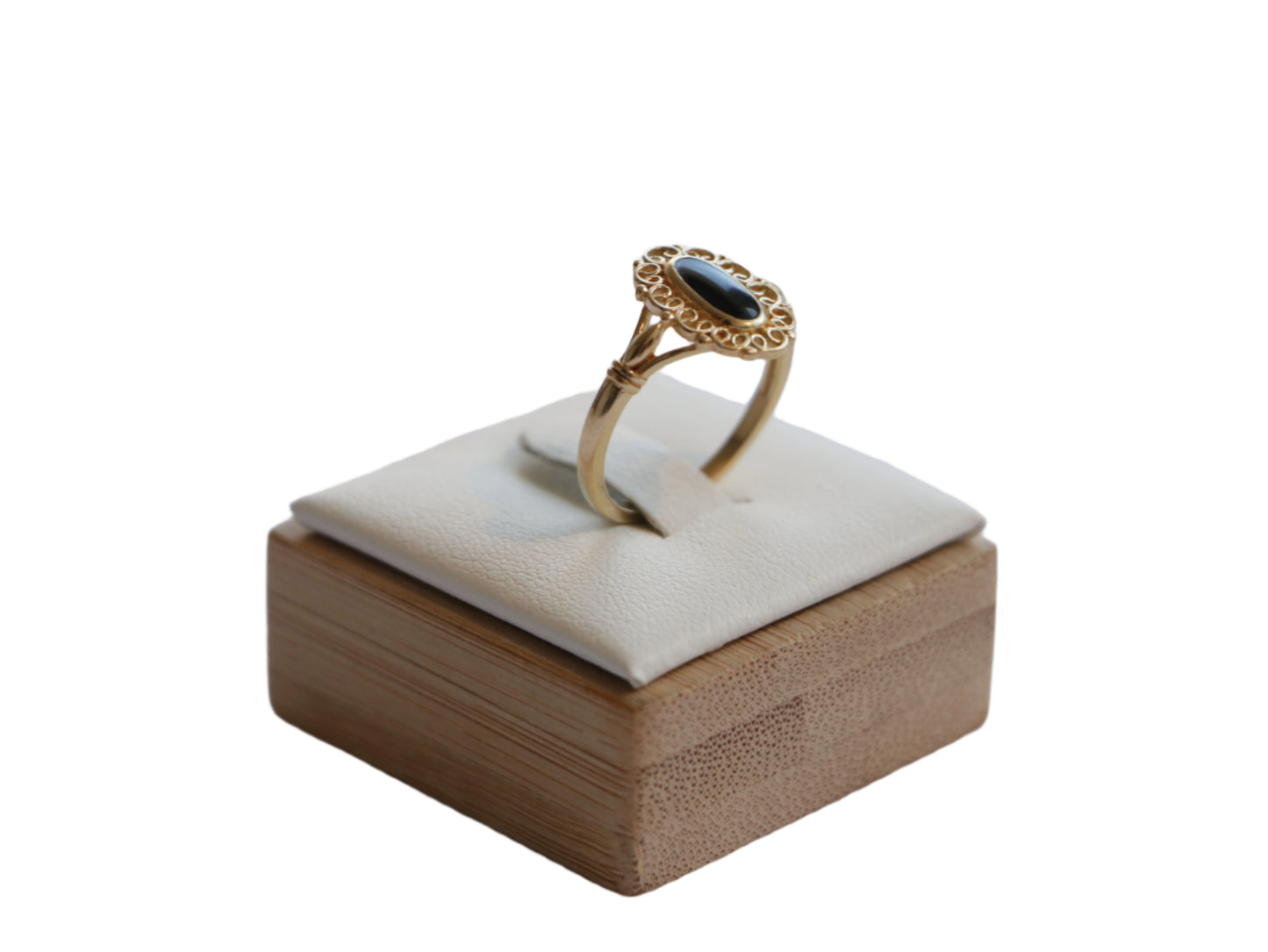 טבעת SOLE RING זהב עם אבן אובלית כהה ועיטור פילגרין, מבט צדדי על מעמד עץ מרופד.