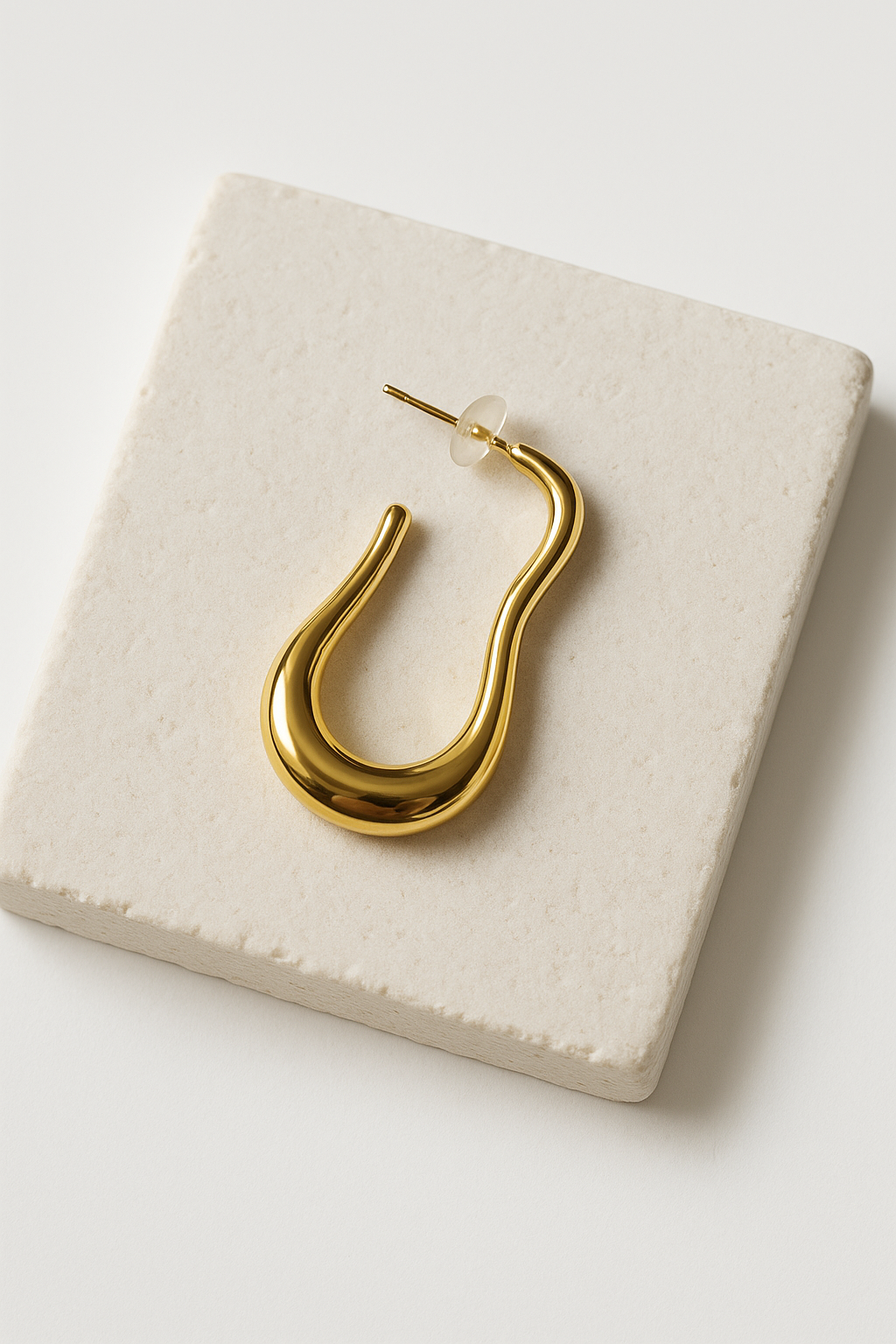 עגיל HILI בודד מזהב מבריק, בעיצוב גלי אורגני, מונח באלכסון על אריח. רואים את מוט הסוגר.