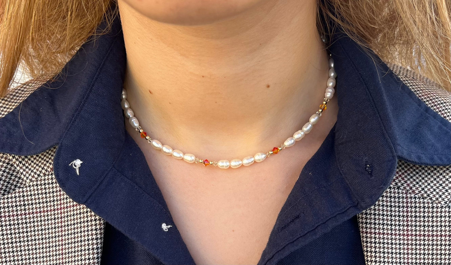 שרשרת ALAMOR APROL GOLD פנינים, חרוזי זהב וחרוזי קריסטל כתומים על דוגמנית, מבט תקריב.