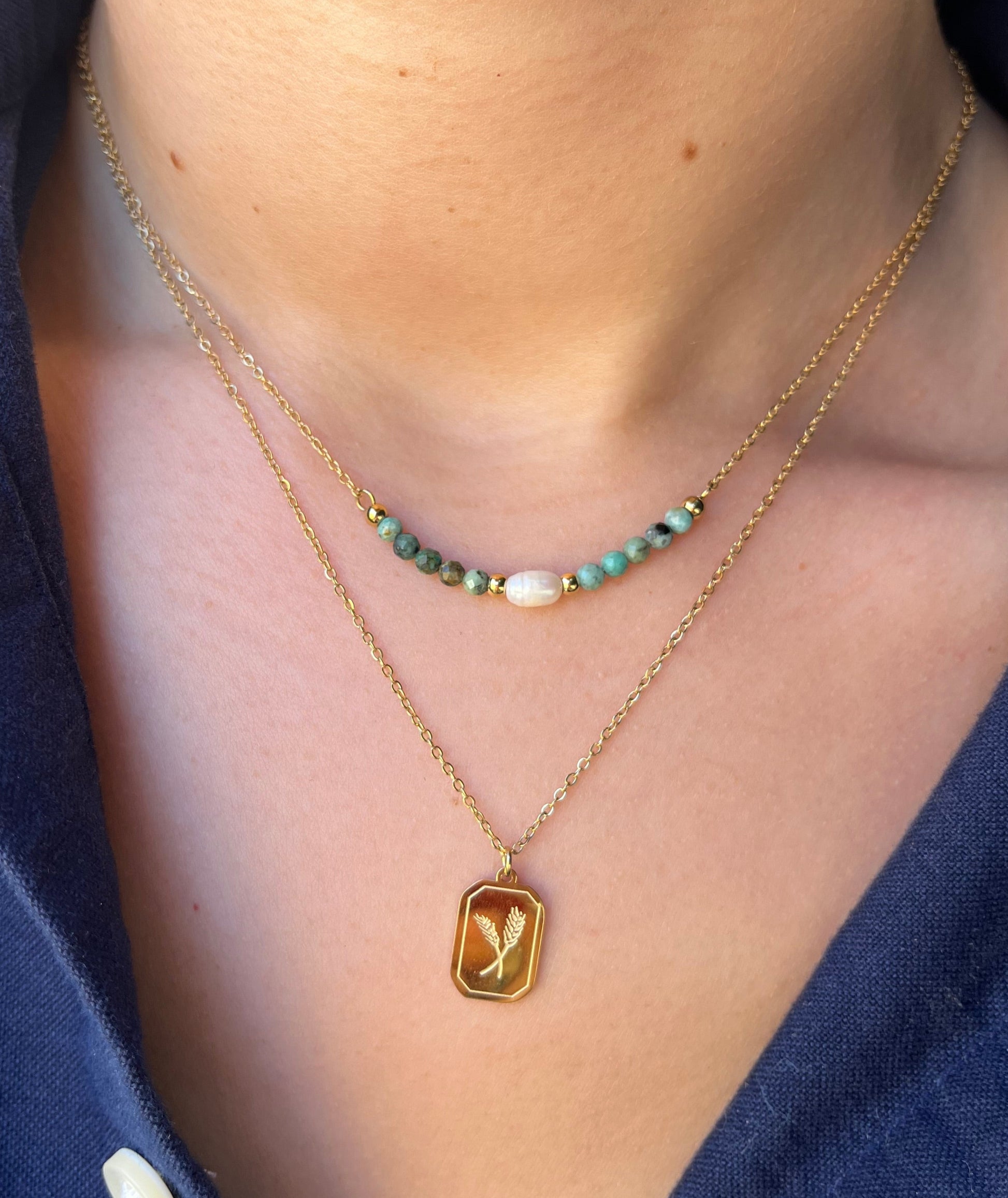 שרשרת LUNARIA כפולה מזהב על דוגמנית. תקריב: פנינה, חרוזי טורקיז ותליון מלבני עם שיבולים.