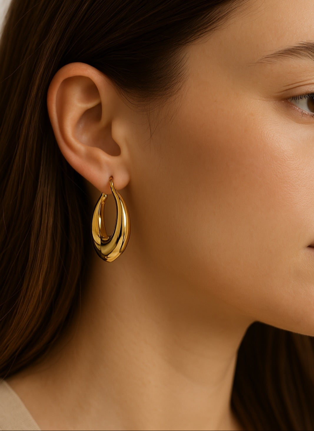 עגיל ALMOG EARRINGS GOLD עבה ומבריק על אוזן דוגמנית, תקריב המדגיש את צורתו הטיפתית המודרנית.