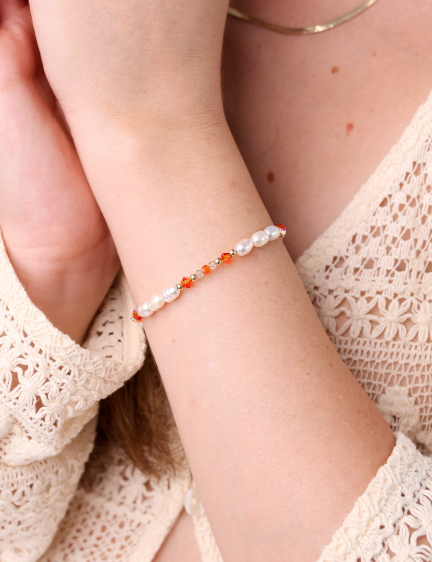 צמיד ALAMOR APROL GOLD על יד דוגמנית, מבט תקריב על פנינים וחרוזים כתומים זוהרים, עם רקע סרוג בהיר.