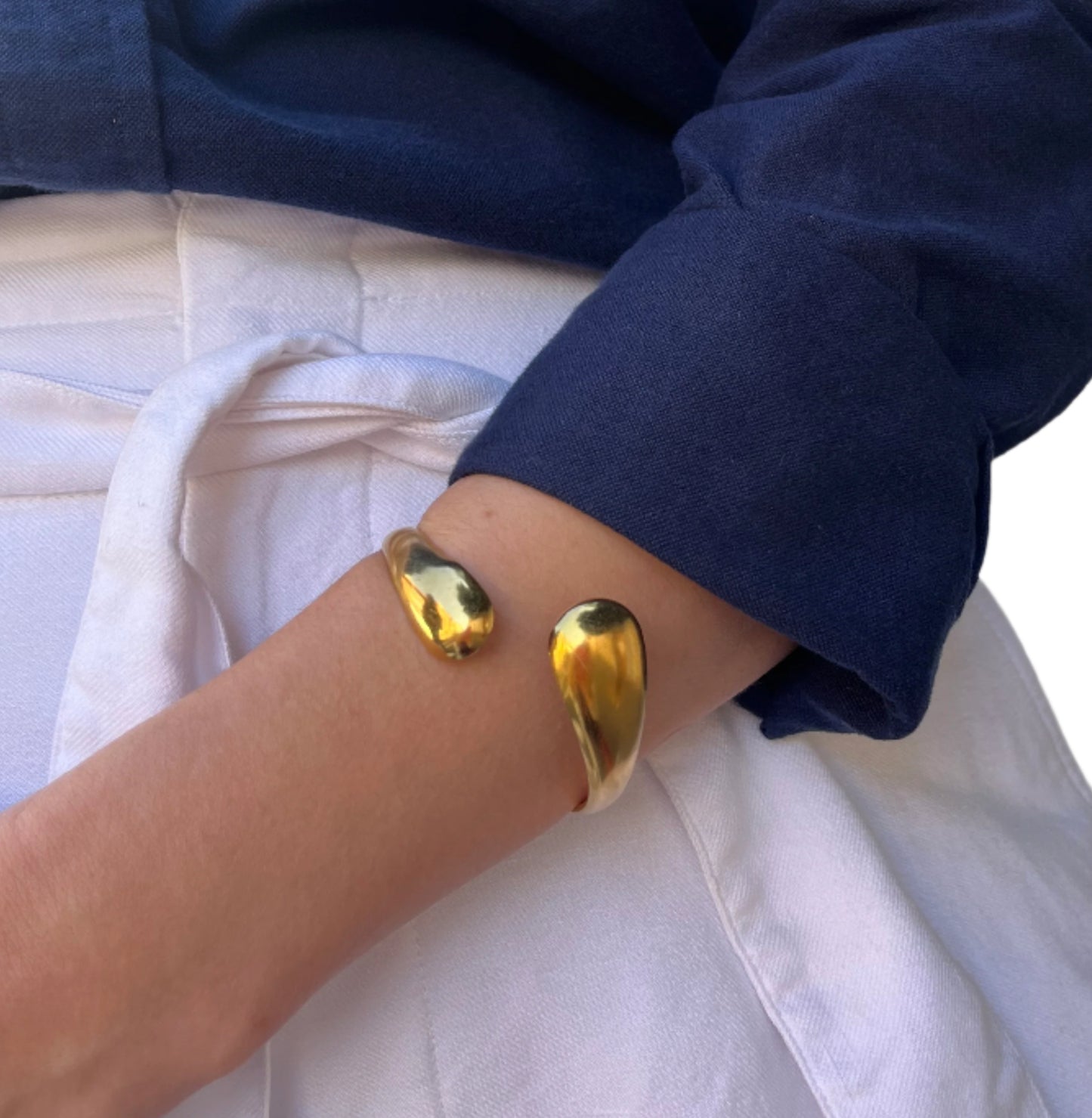 צמיד ETERNA BRACELET זהב מבריק, עם קצוות מלוטשים דמויי טיפה, ענוד על זרוע דוגמנית בלבוש כחול-לבן.