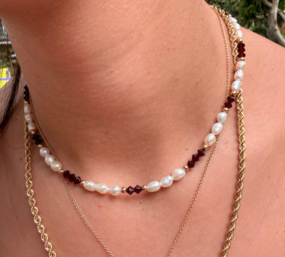 שרשרת ALAMOR BORDEAUX GOLD NECKLACE עם פנינים וחרוזי בורדו על צוואר דוגמנית, בשילוב שרשראות זהב בשכבות.