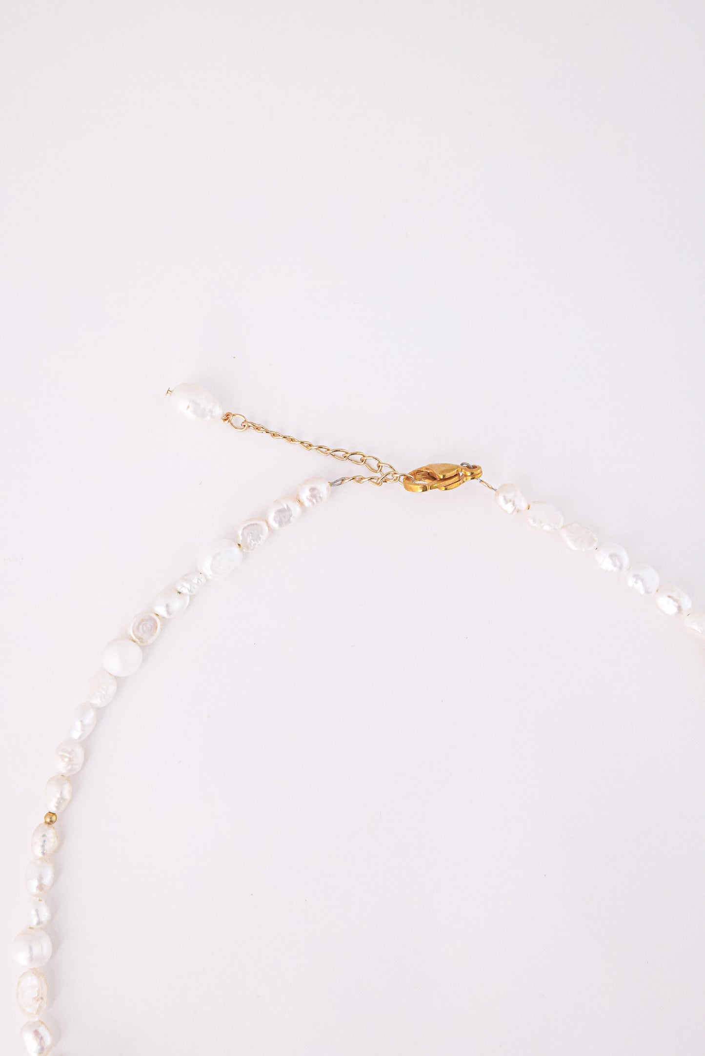 שרשרת SHAI NECKLACE של Lidi. תקריב על סוגר זהב, שרשרת הארכה ופניני בארוק עם חרוז זהב קטן.