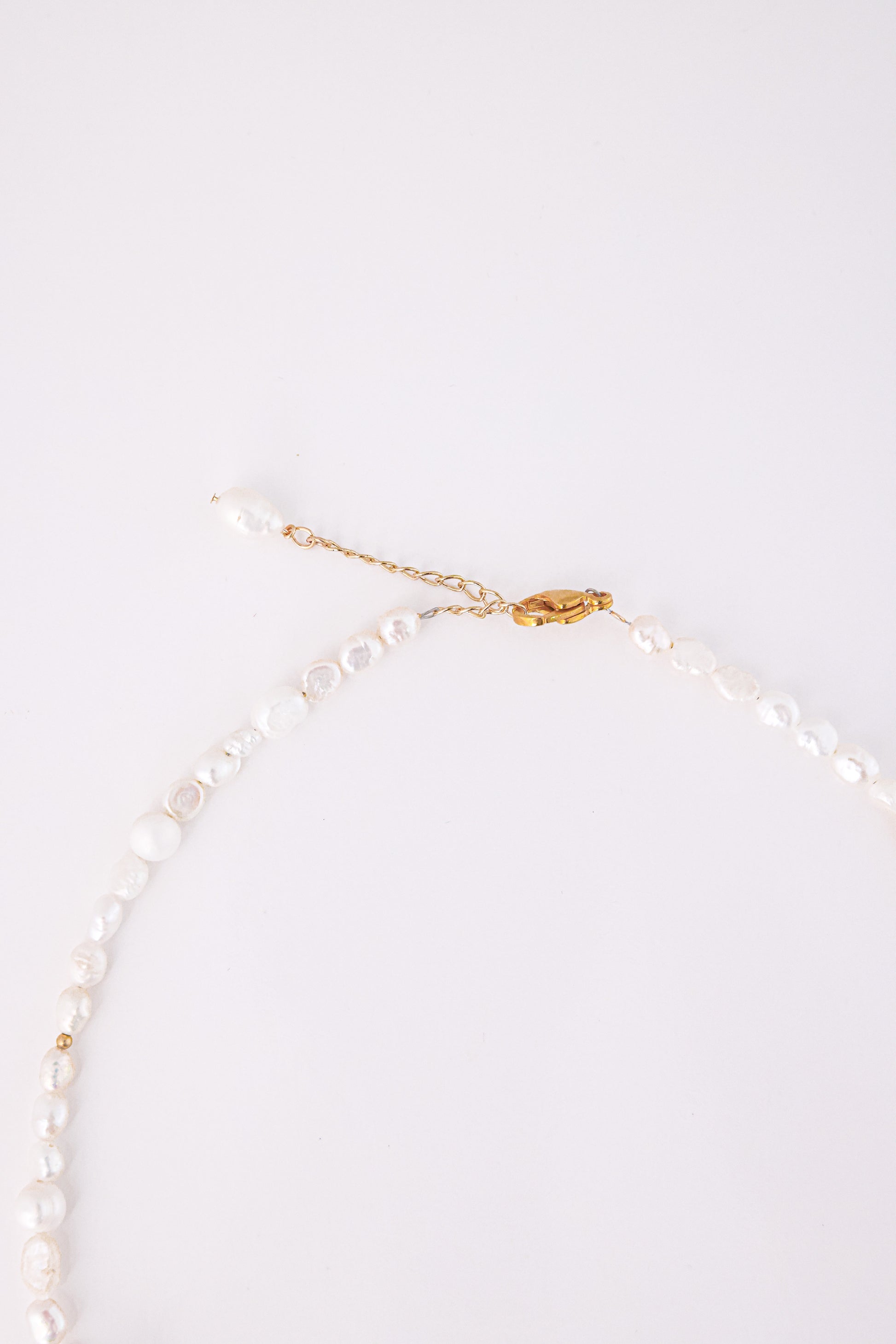 שרשרת SHAI NECKLACE של Lidi. תקריב על סוגר זהב, שרשרת הארכה ופניני בארוק עם חרוז זהב קטן.