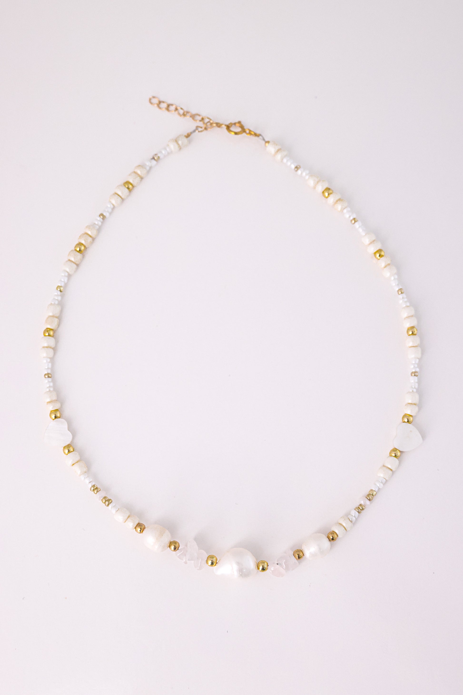 שרשרת LIHI NECKLACE, מבט עליון על חרוזי פנינים טבעיות, שבבי קוורץ ורוד, חרוזי לבבות וחרוזי זהב, על רקע לבן.