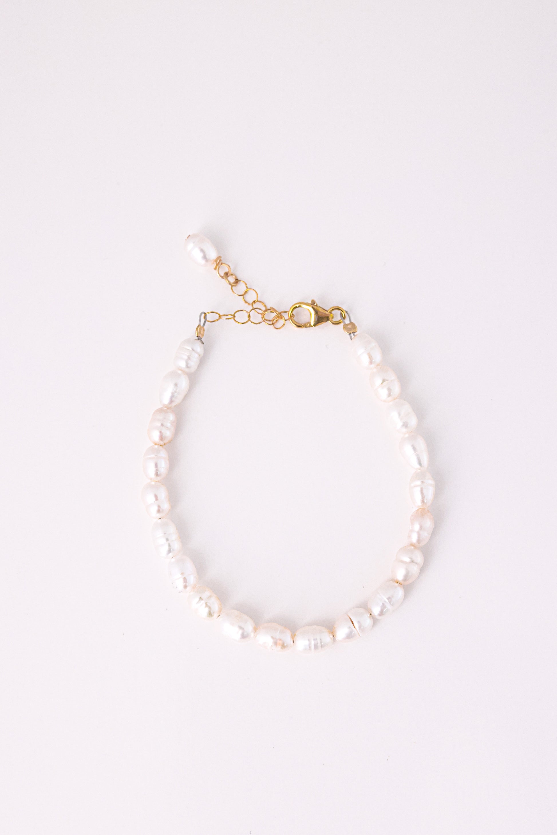 צמיד ANNA BRACELET GOLD, פנינים לבנות לא סדורות, סוגר ושרשרת הארכה מזהב, מצולם מלמעלה על רקע לבן.