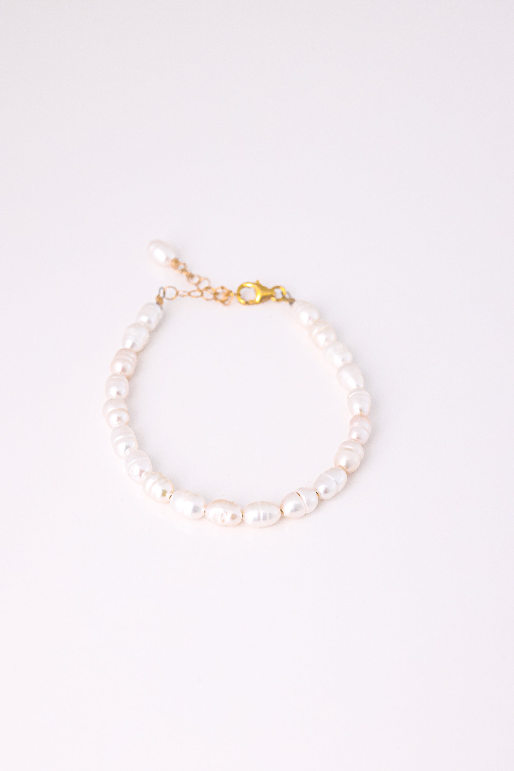 צמיד ANNA BRACELET GOLD פנינים לבנות אובליות, מונח במעגל על רקע לבן, סוגר ושרשרת הארכה מזהב.