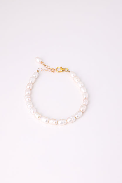 צמיד ANNA BRACELET GOLD פנינים לבנות אובליות, מונח במעגל על רקע לבן, סוגר ושרשרת הארכה מזהב.