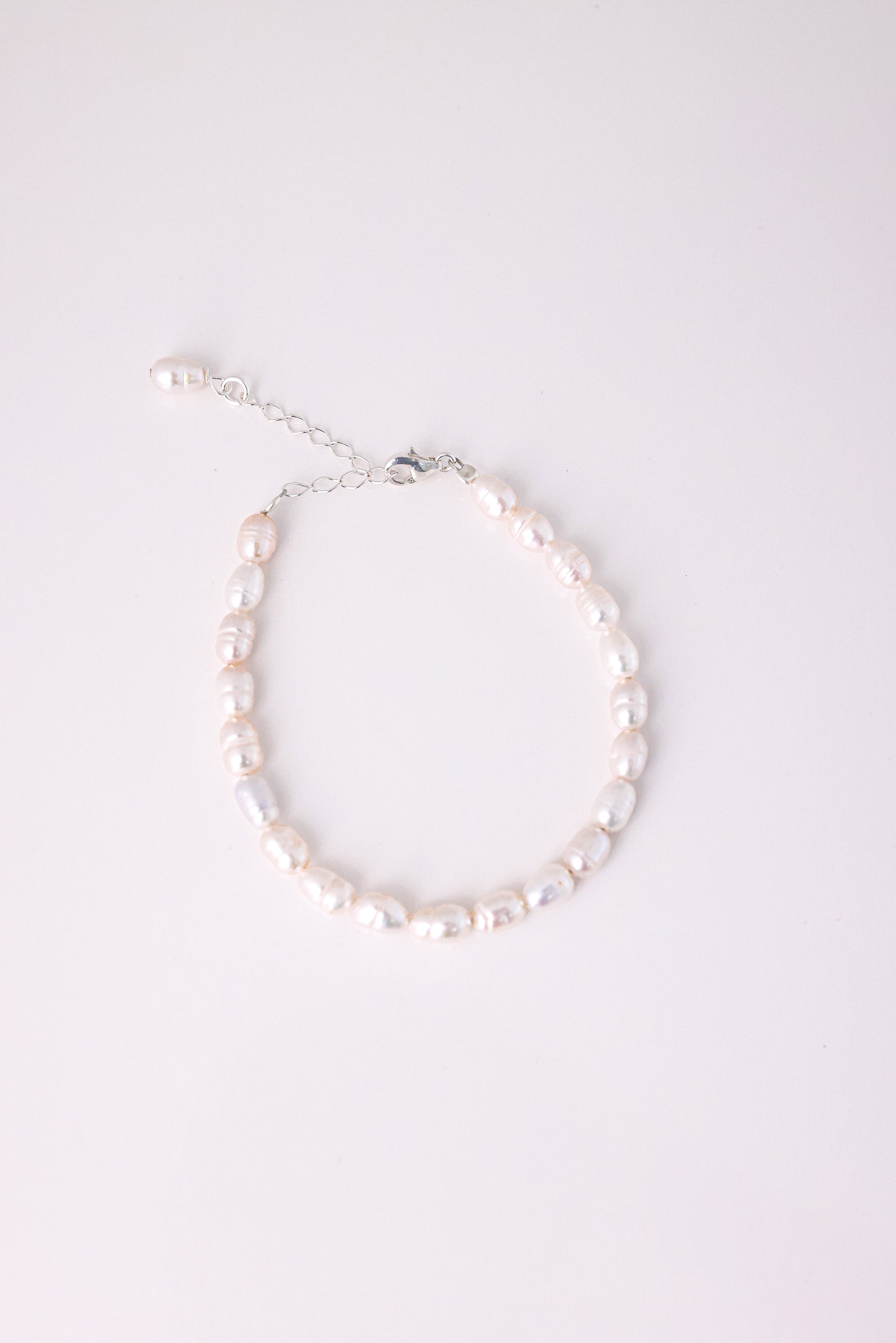 צמיד ANNA BRACELET SILVER פנינים מתורבתות לא סדירות בגוון ורדרד, מצולם מלמעלה עם סוגר ושרשרת הארכה כסופים על רקע לבן.