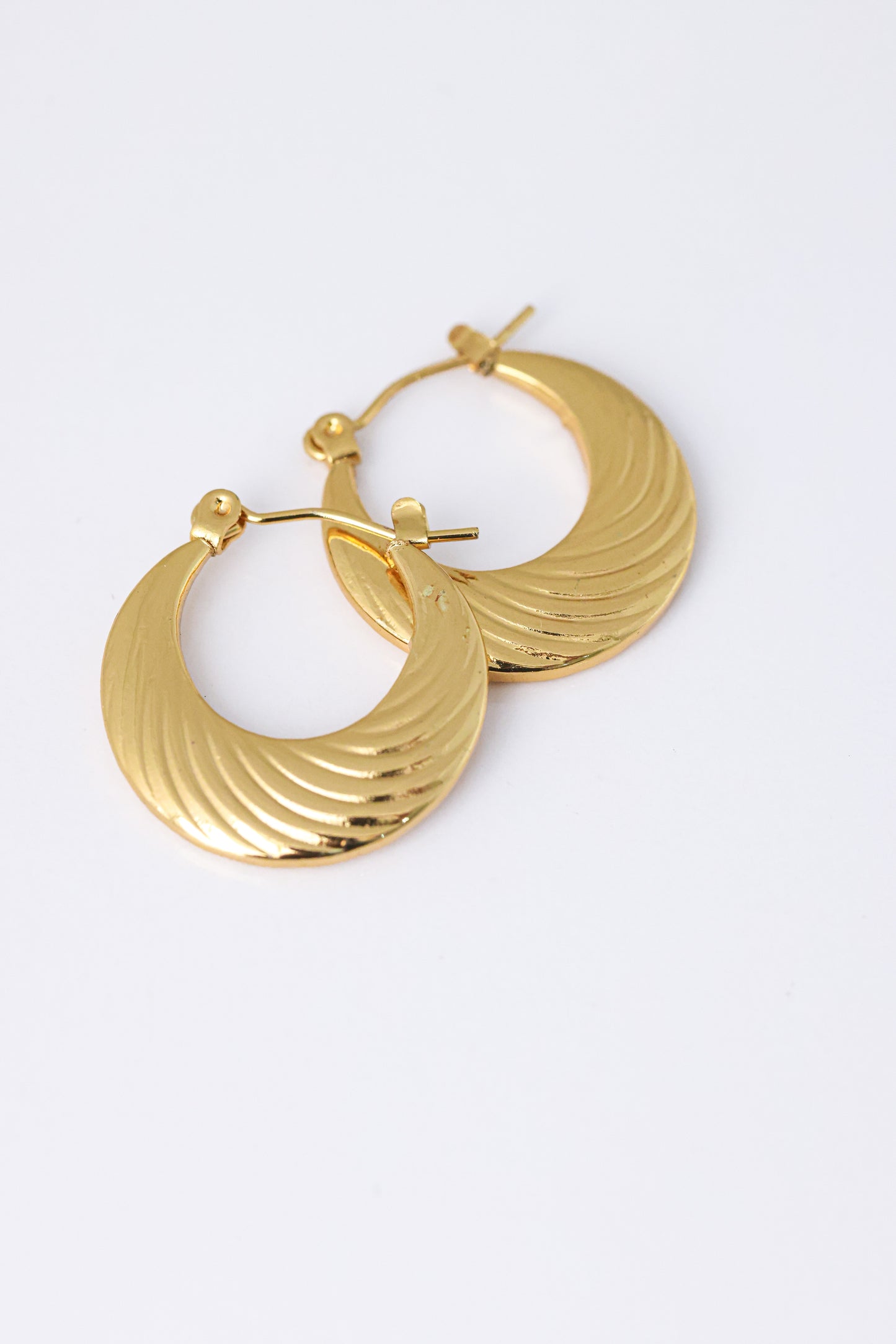זוג עגילי חישוק שטוחים ורחבים MIKA EARRINGS מזהב, עם טקסטורת גלים עדינה, מצולמים מלמעלה על רקע לבן.