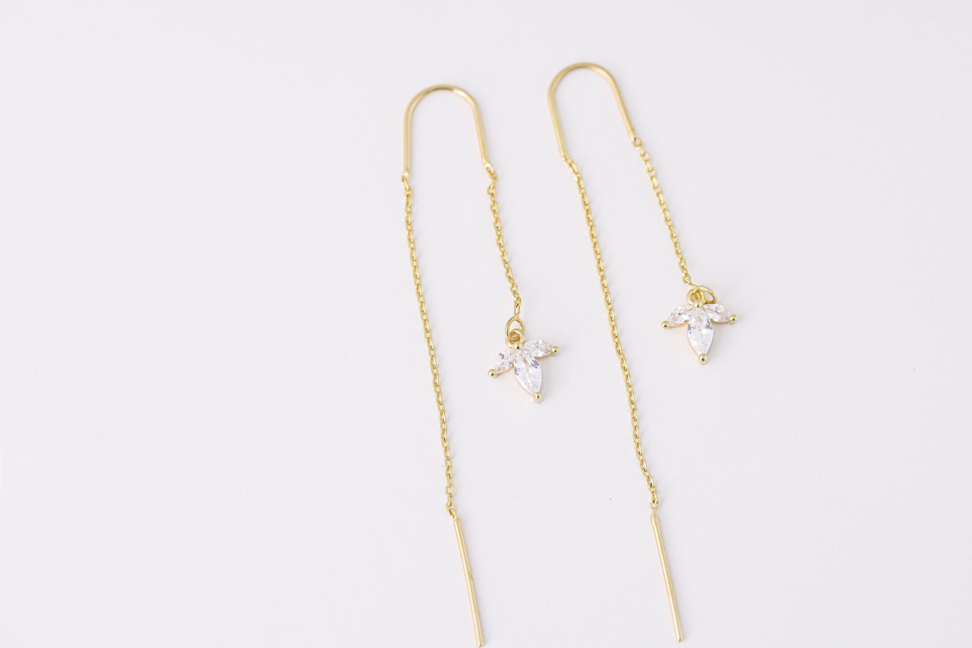 עגילי SARAI מזהב, עיצוב נשפך עם תליון פרח משלוש אבני זירקוניה שקופות. צילום מלמעלה על רקע לבן, מבט מלא.