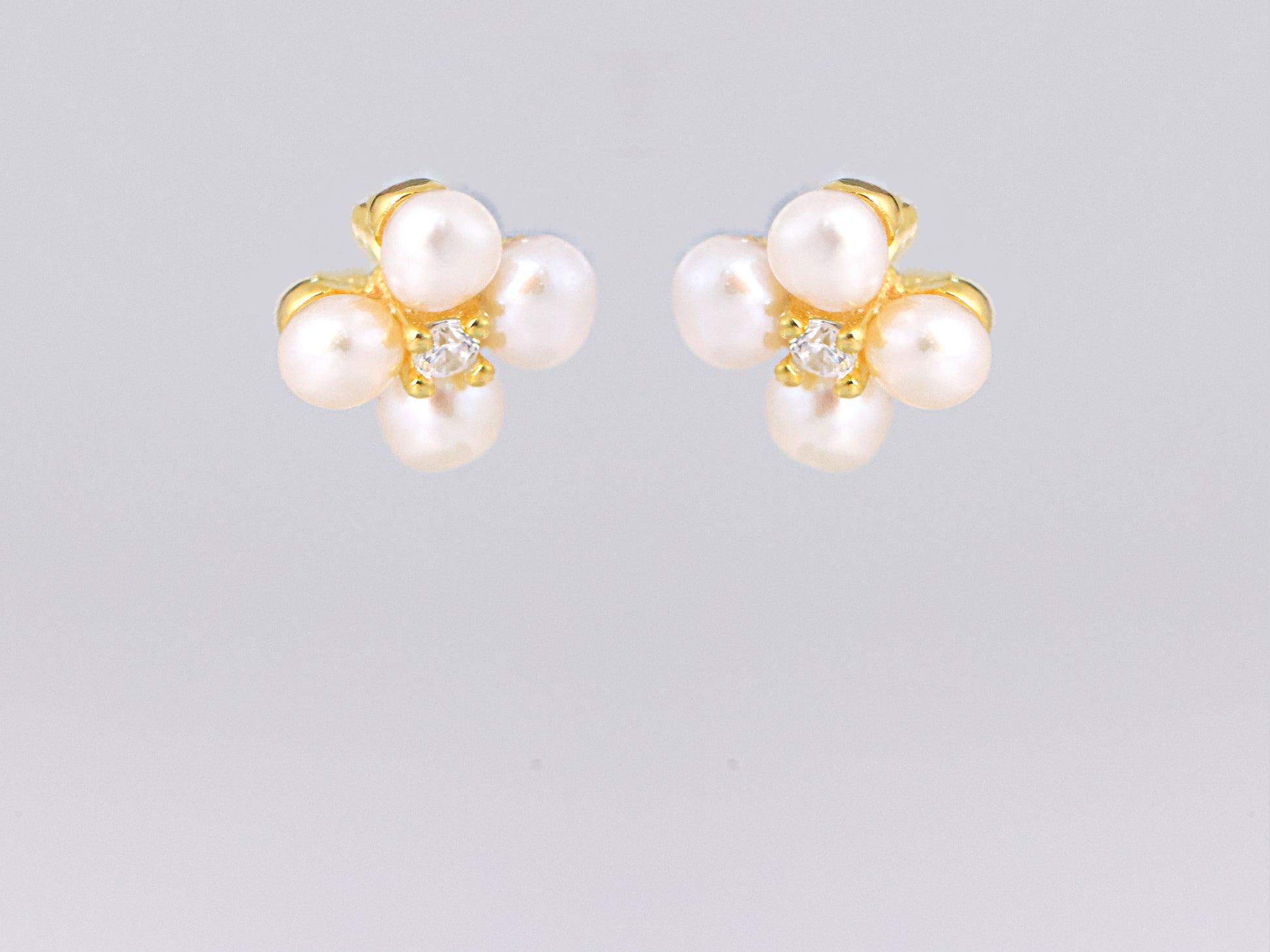 עגילי NOA EARRINGS GOLD מזהב, מבט מלפנים על תלתן פנינים לבנות ואבן נוצצת במרכז.
