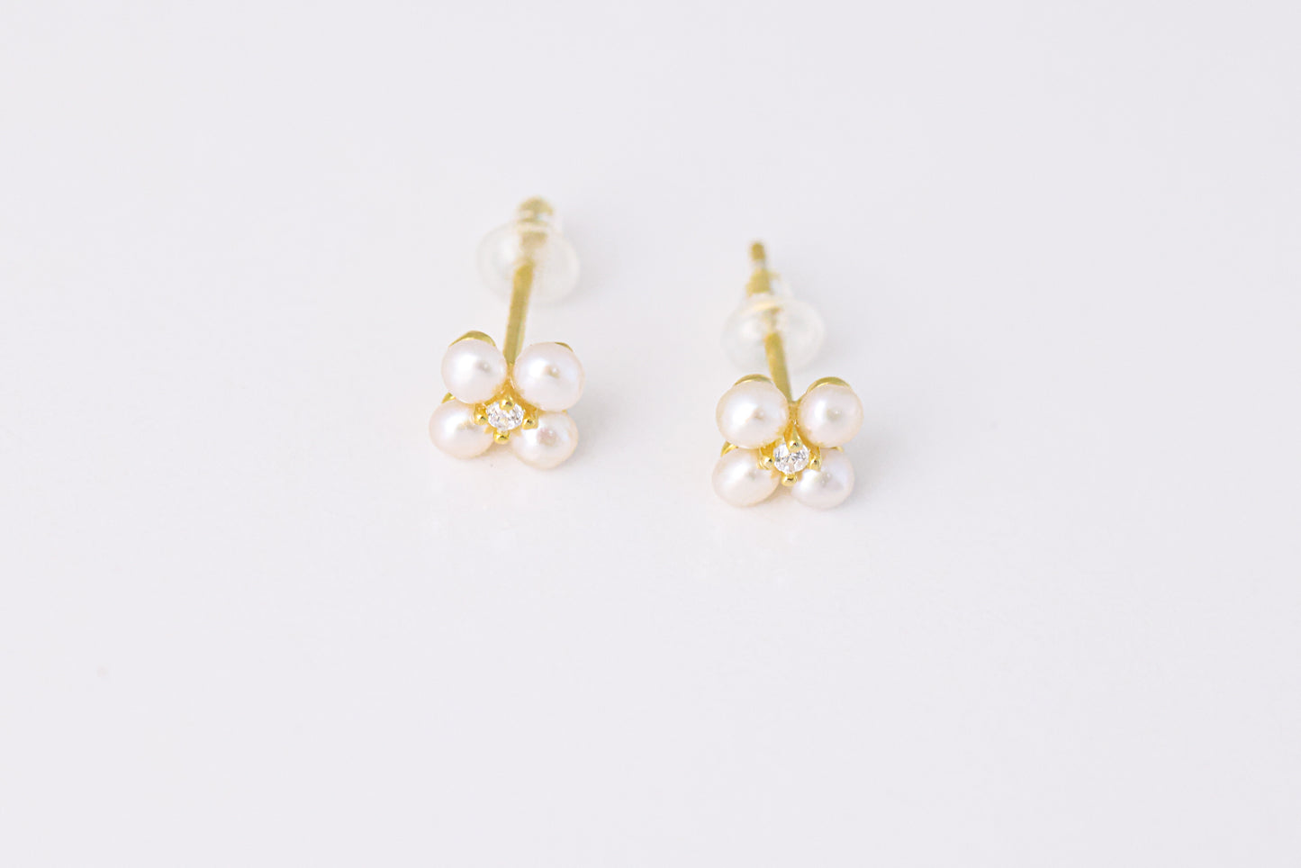 זוג עגילי NOA EARRINGS GOLD צמודים, זהב עם 4 פנינים זעירות ויהלום במרכז, מצולמים מלמעלה על רקע לבן.