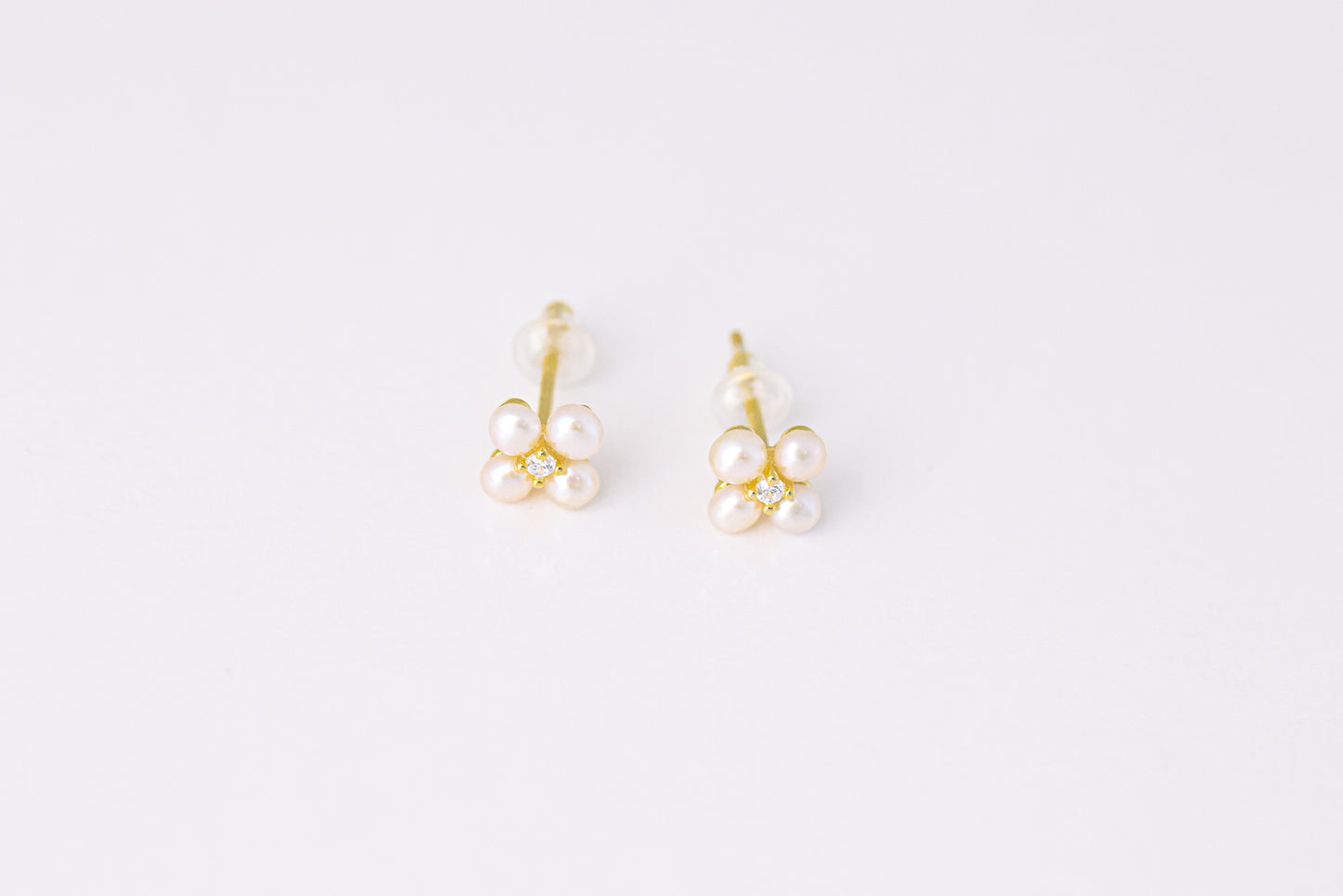 עגילי NOA EARRINGS GOLD, תקריב של זוג עגילים מזהב, כל אחד פרח מ-4 פנינים ויהלום במרכז, על רקע לבן.