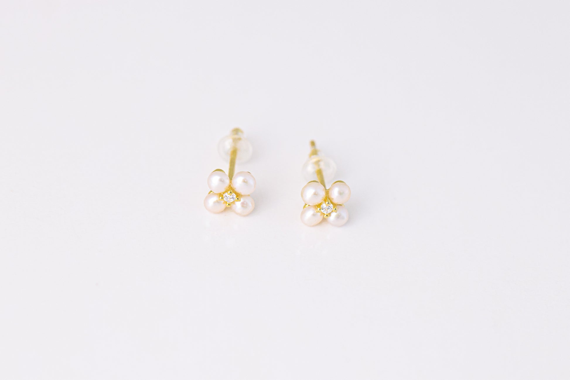 עגילי NOA EARRINGS GOLD, תקריב של זוג עגילים מזהב, כל אחד פרח מ-4 פנינים ויהלום במרכז, על רקע לבן.