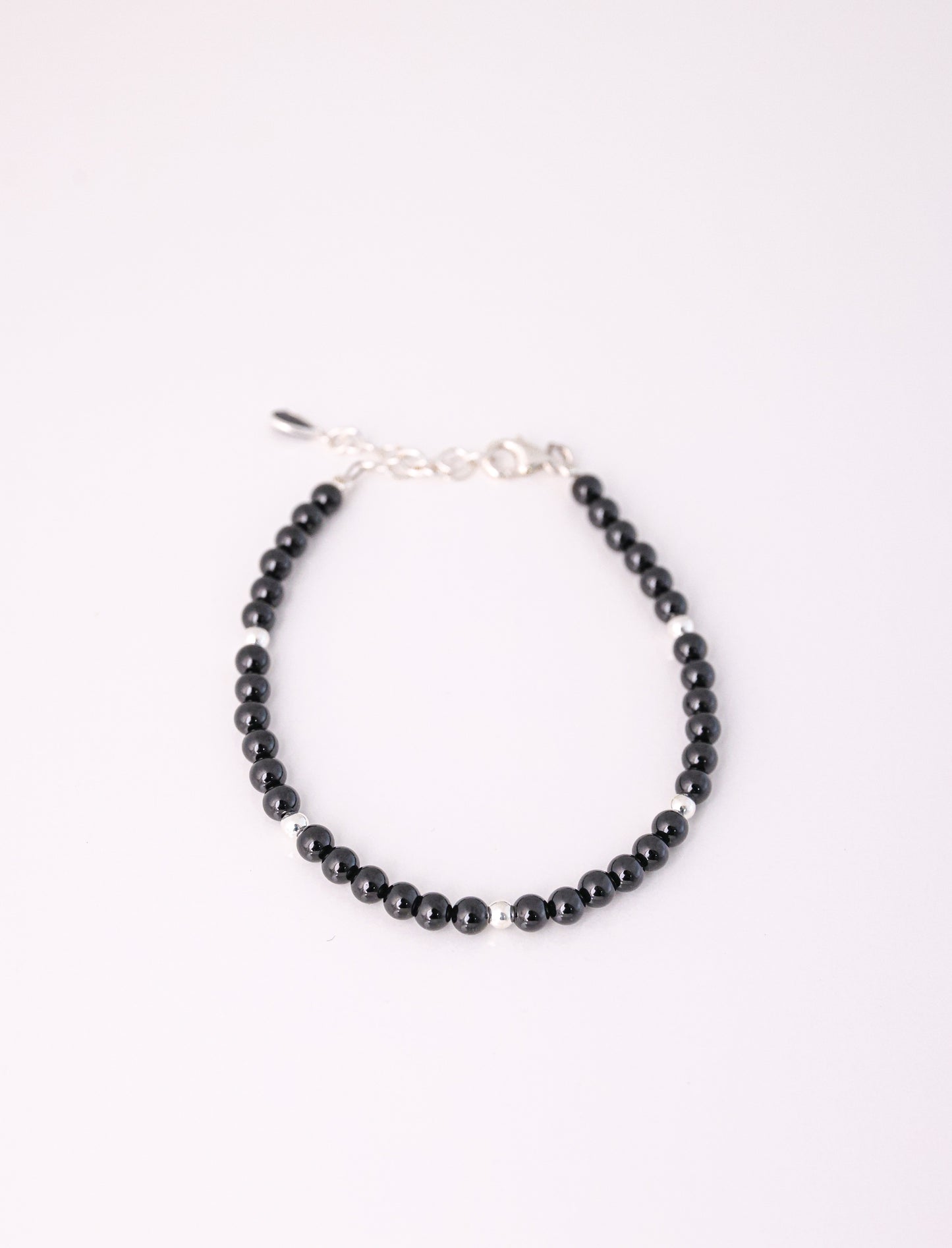 צמיד RONA BRACELET חרוזים שחורים מבריקים וכדורי כסף מפרידים, מבט מלמעלה על רקע לבן. כולל סוגר אבזם ושרשרת הארכה.