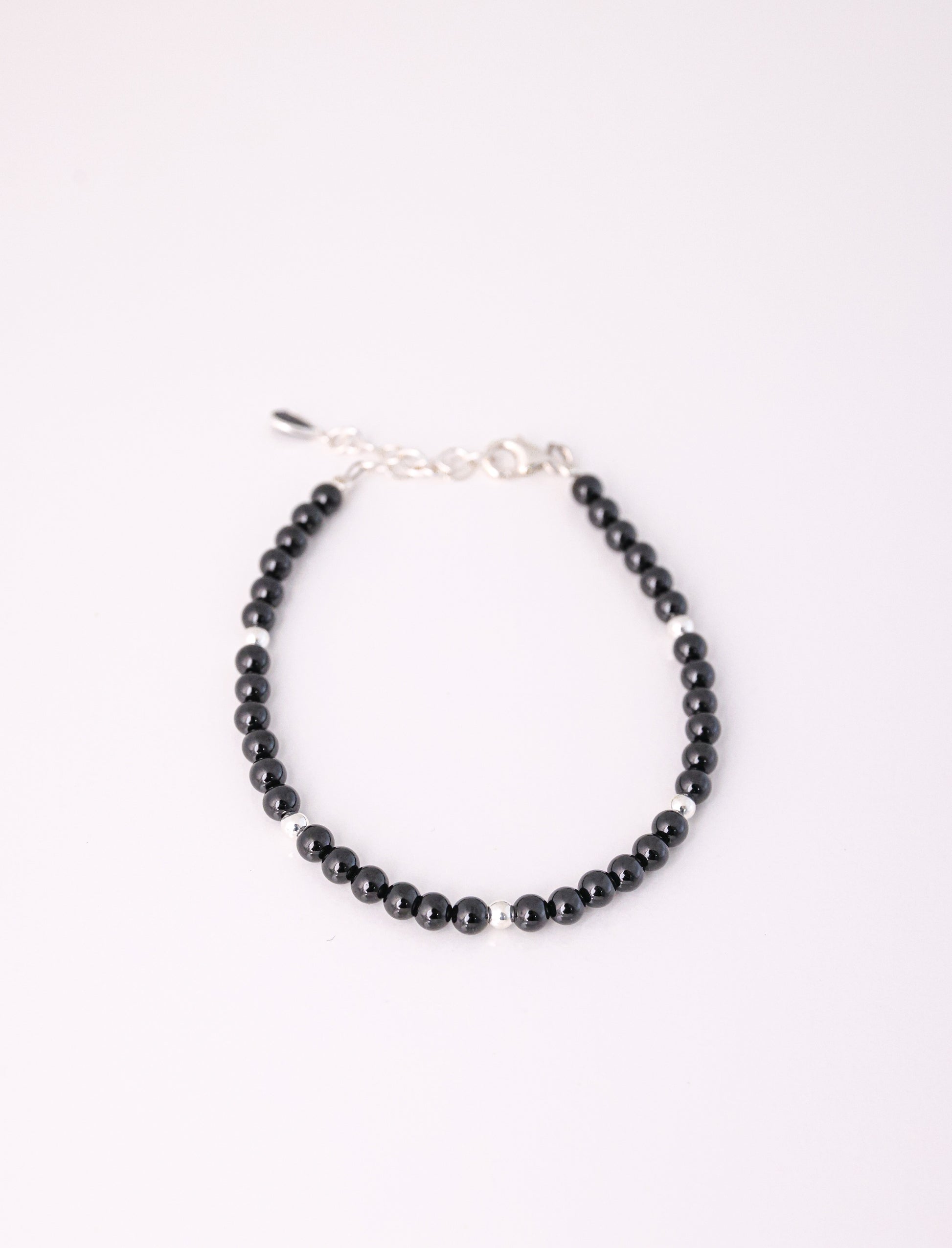 צמיד RONA BRACELET חרוזים שחורים מבריקים וכדורי כסף מפרידים, מבט מלמעלה על רקע לבן. כולל סוגר אבזם ושרשרת הארכה.