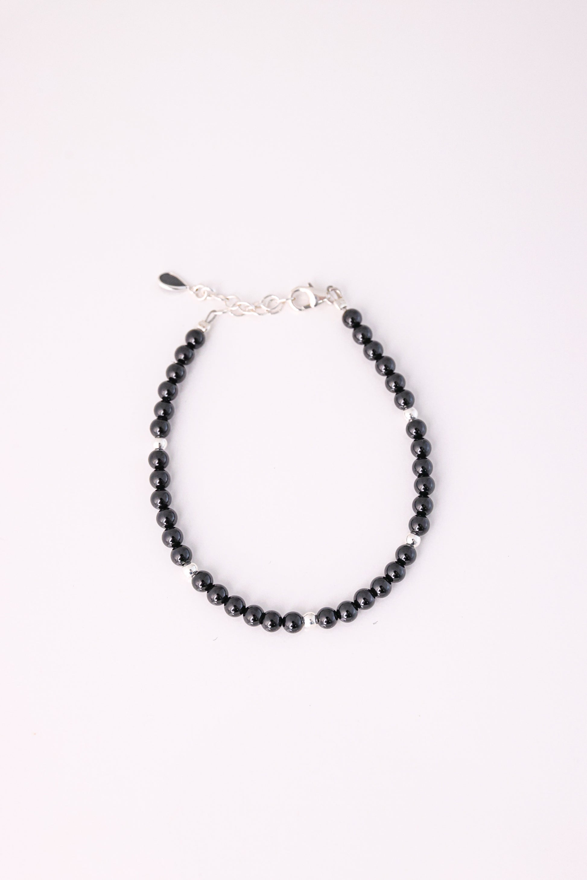 צמיד RONA מעוצב מחרוזים שחורים מבריקים עם חרוז כסף בודד, סוגר ושרשרת הארכה כסופים, מצולם מלמעלה על רקע לבן.