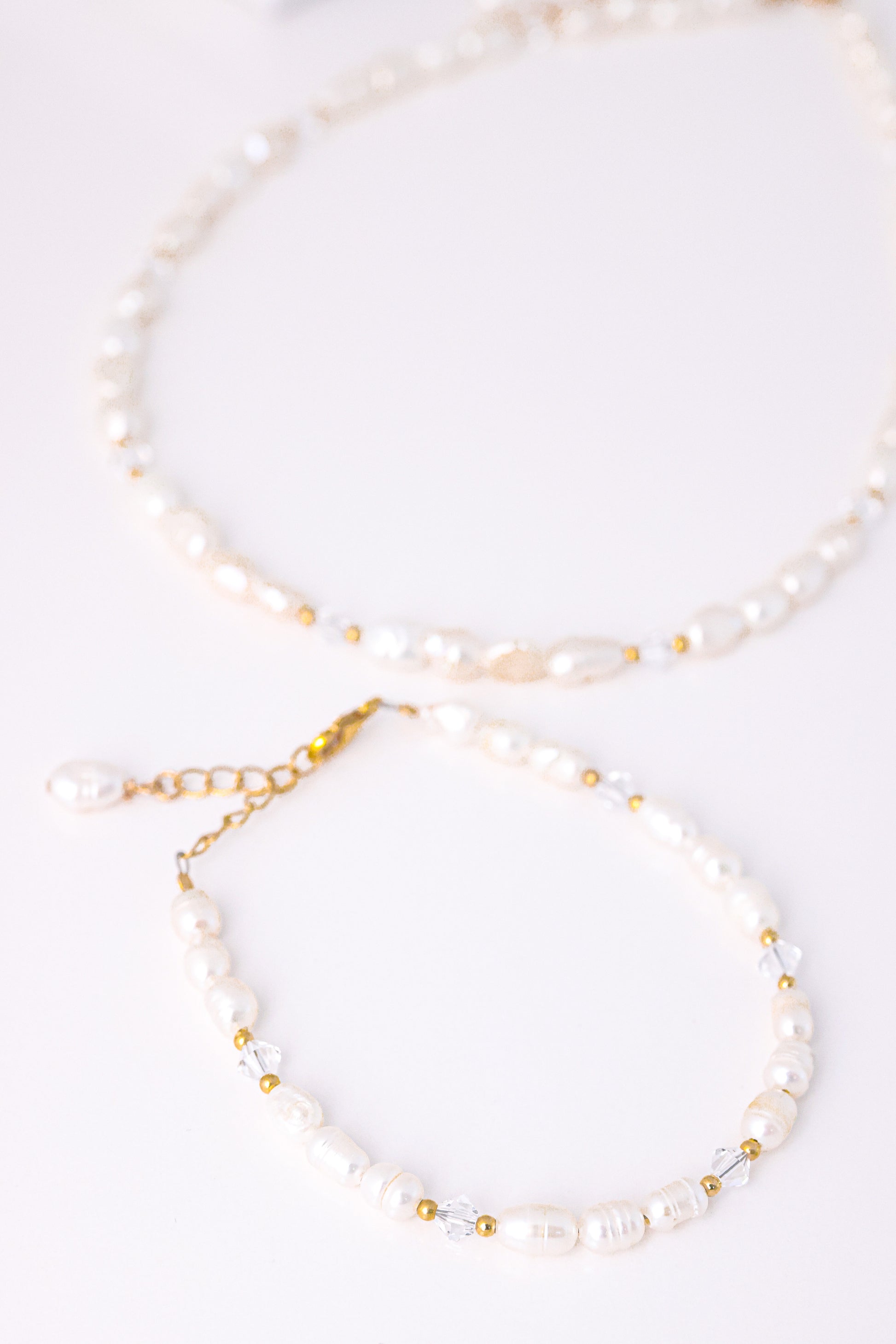 סט תכשיטי ALAMOR QUARTZ GOLD. צמיד פנינים וחרוזי קוורץ שקופים בתקריב עם סוגר זהב, שרשרת תואמת ברקע.