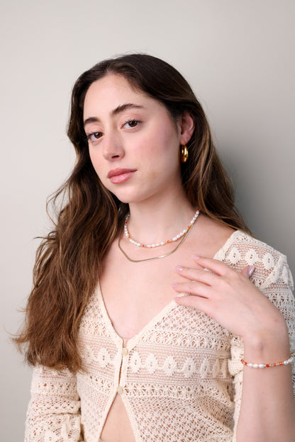 דוגמנית עונדת סט ALAMOR APROL GOLD: שרשרת פנינים וכתום משולבת זהב, צמיד תואם, וידה על חזה.