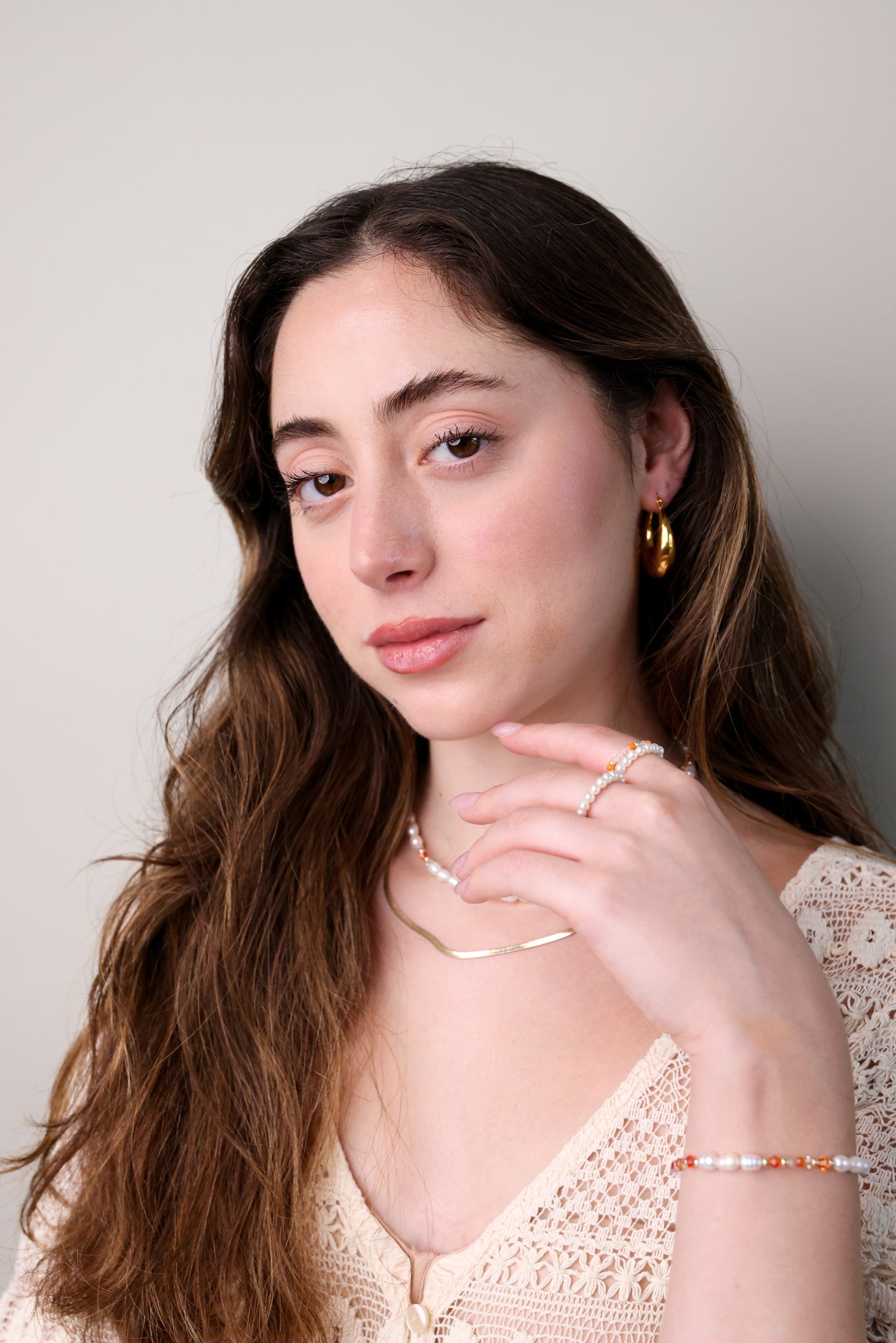 דוגמנית עונדת שרשרת ALAMOR APROL GOLD פנינים וחרוזים מוזהבים, יד מלטפת צוואר, תקריב.