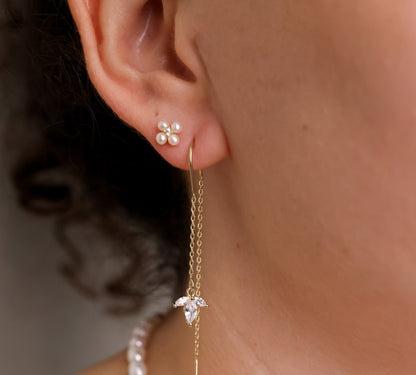 עגילי NOA EARRINGS GOLD על אוזן דוגמנית, תקריב: עגיל שרשרת זהב עם קריסטלים דמויי עלים, לצד עגיל צמוד פנינים.