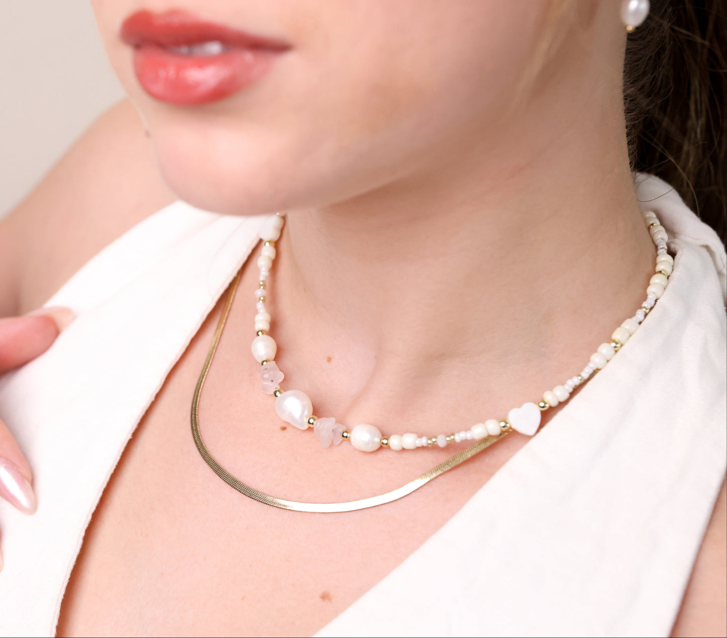 שרשרת LIHI NECKLACE כפולה על צוואר דוגמנית: שרשרת נחש זהובה ושרשרת פנינים, אבני רוז קוורץ וחרוזים. מבט תקריב.