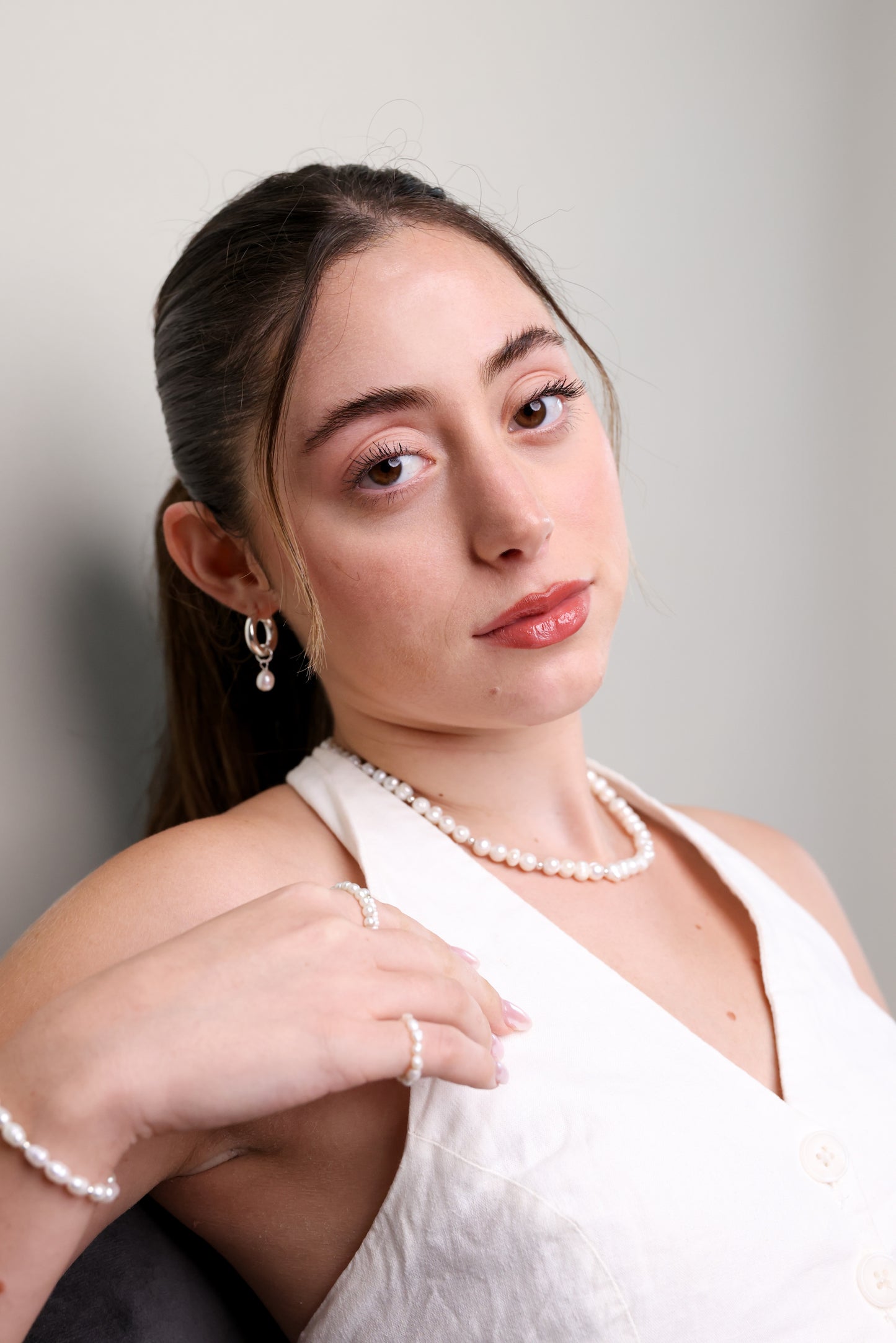 דוגמנית בחולצה לבנה, מביטה למצלמה, עונדת שרשרת GEFEN פנינים, טבעת וצמיד תואמים.