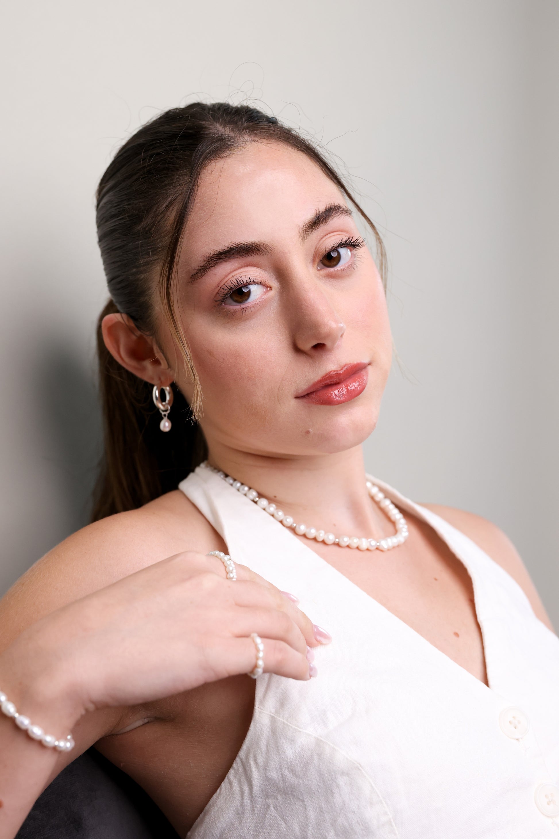 דוגמנית בחולצה לבנה, מביטה למצלמה, עונדת שרשרת GEFEN פנינים, טבעת וצמיד תואמים.