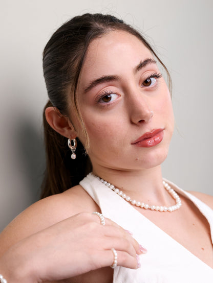 דוגמנית עם עגילי PEARL S SILVER חישוק ופנינה, שרשרת פנינים וטבעות תואמות, במבט ישיר, לבושה לבן.